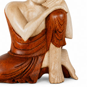 Gros plan sur les détails sculptés et le vêtement de la statue Bouddha pensif en bois de Suar