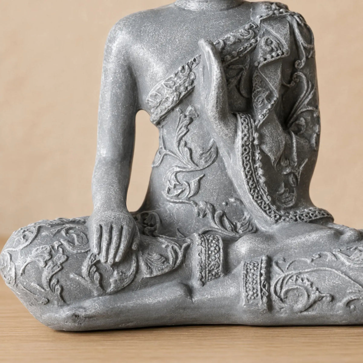Gros plan sur les mains, la robe sculptée et la finition effet pierre de la statuette Bouddha