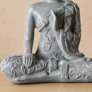 Gros plan sur les mains, la robe sculptée et la finition effet pierre de la statuette Bouddha